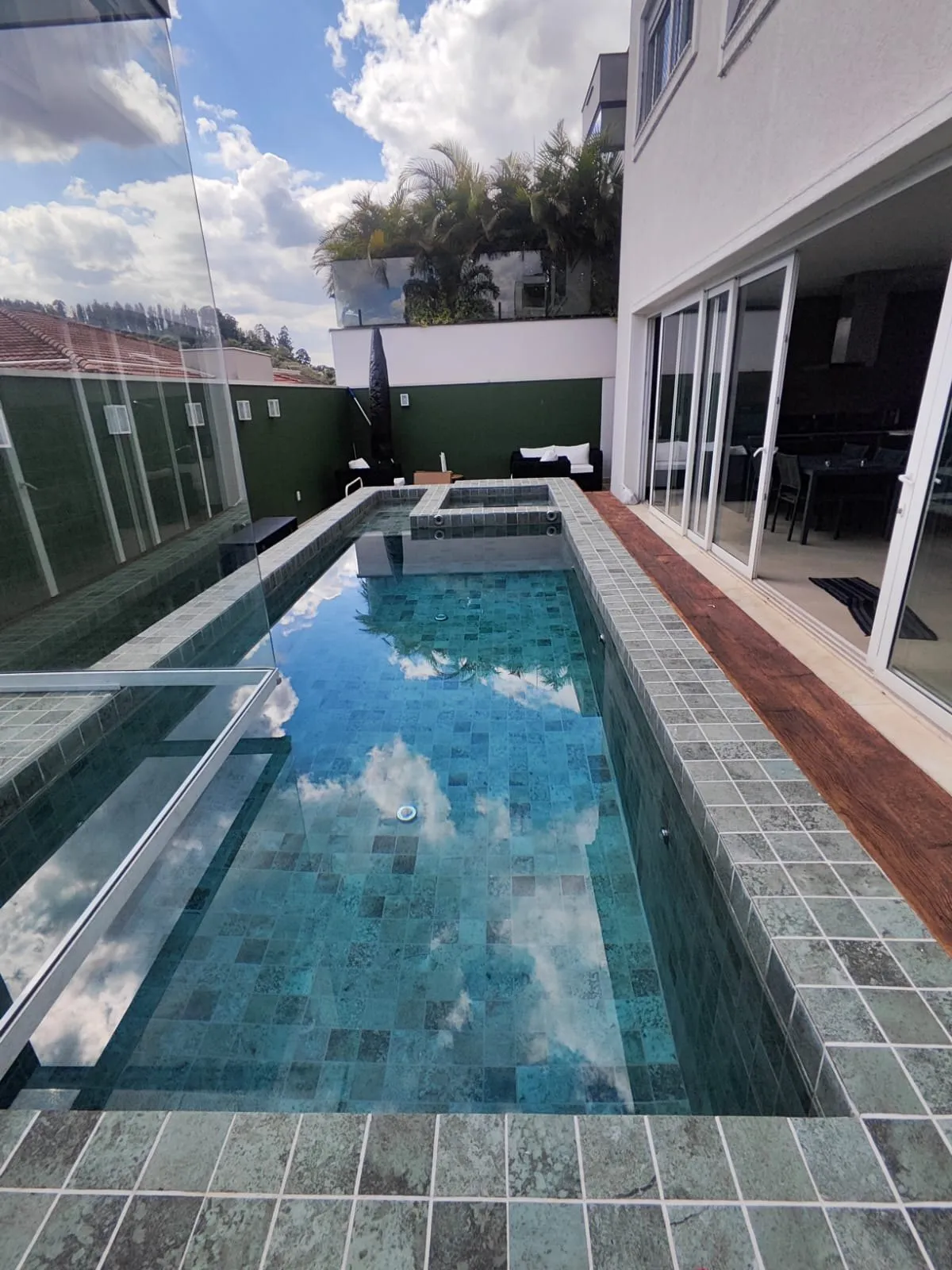 Piscina longa com revestimento verde e deck de madeira
